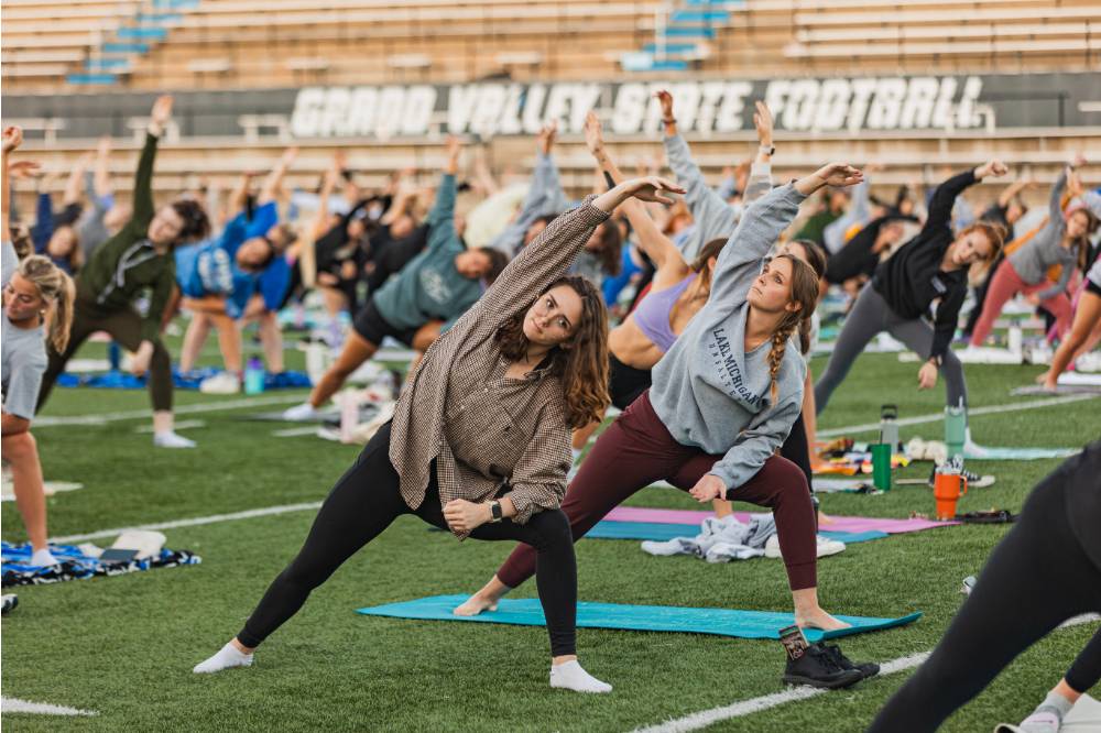 students standing and stretching during yoga on the football field at sunset